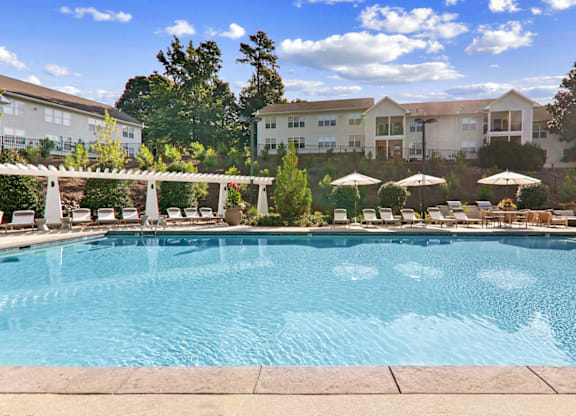 a swimming pool with lounge chairs and umbrellas in front of a building at Caveness Farms Apartments, Wake Forest 