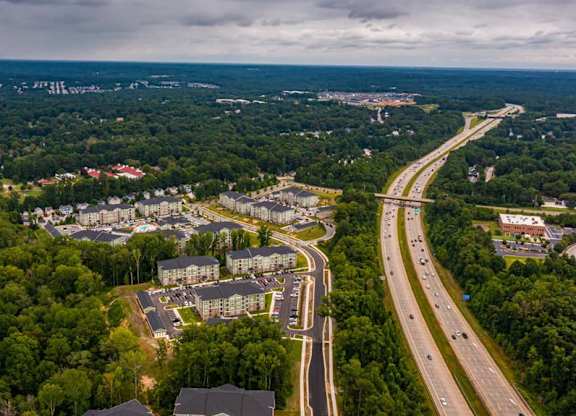 A highway cuts through a wooded area with a large building to the left at Foxwood Apartments, North Carolina, 27616