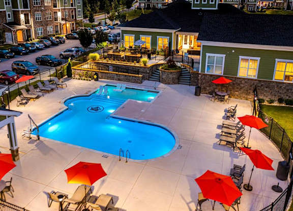 A swimming pool surrounded by red umbrellas and lounge chairs at Foxwood Apartments, Raleigh-Durham