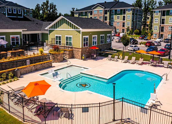 A pool surrounded by a black fence with orange umbrellas at Foxwood Apartments, North Carolina, 27616