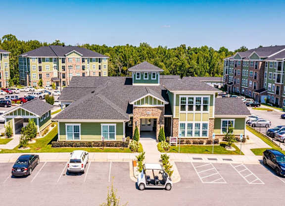 A parking lot with cars and a golf cart in front of a building with a green roof at Foxwood Apartments, North Carolina, 27616