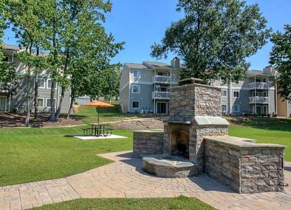 an outdoor fireplace with a fire pit in the middle of a grassy area with an apartment at Eastchester Ridge Apartments, North Carolina, 27262