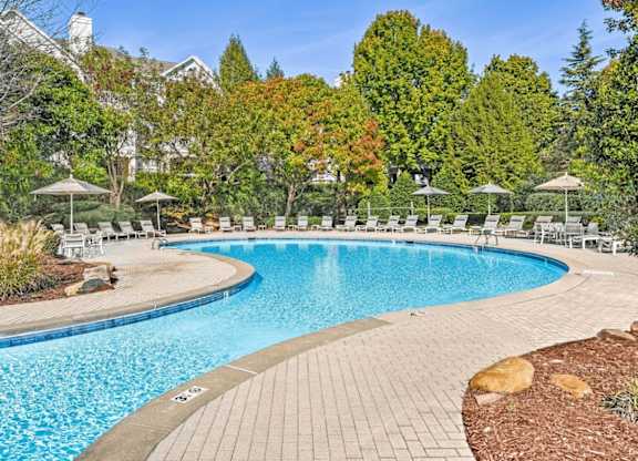 A large outdoor swimming pool surrounded by trees and chairs.