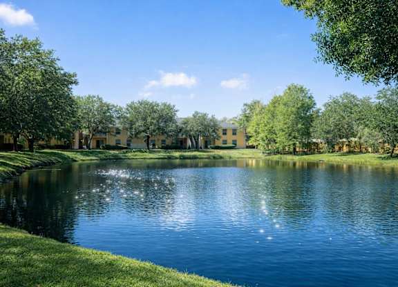 A serene lake surrounded by lush greenery and buildings in the distance.