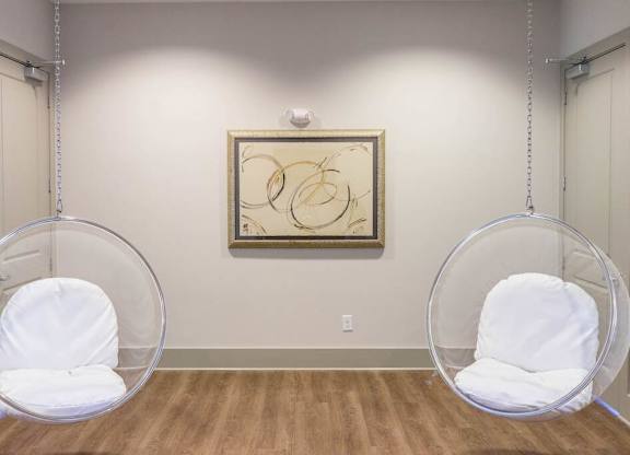 Two white chairs are suspended from the ceiling in a room with a framed artwork on the wall at Foxwood Apartments, North Carolina