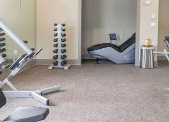 A gym room with a treadmill, weights, and a chair at Foxwood Apartments, Raleigh-Durham