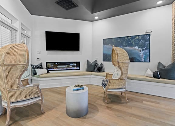 A living room with a flat screen TV mounted on the wall and two wicker chairs facing a white couch at Litchford 315 Apartments, North Carolina