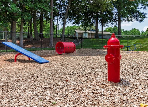 A red fire hydrant sits on a playground with a blue bench and two red barrels at Madison Southpark Apartment Homes, Charlotte, North Carolina