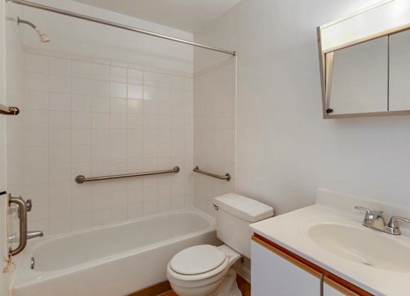 Bathroom with White Cabinets White Counters and White Bathtub and Shower with Handrails