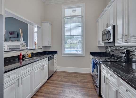 A kitchen with white cabinets and black countertops.