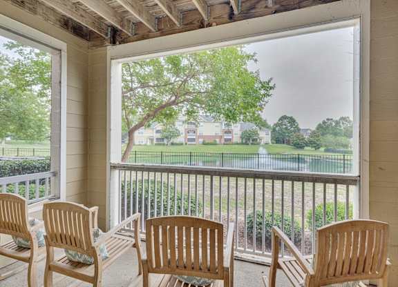 A balcony with four chairs and a view of a green lawn and trees.