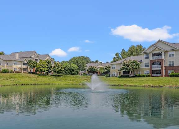 A serene lake in front of a row of houses with a fountain in the middle.