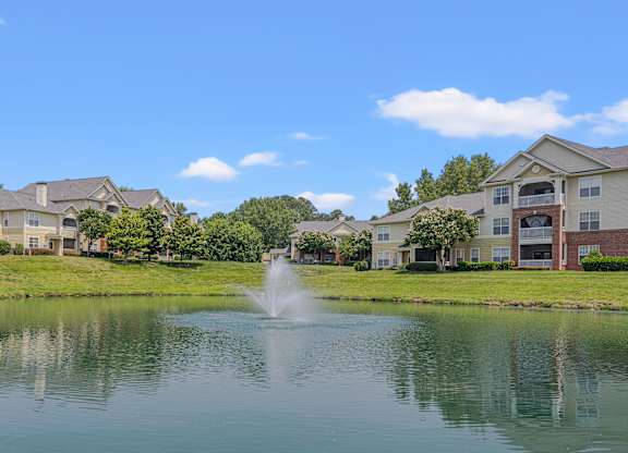 A fountain in the middle of a lake surrounded by houses.