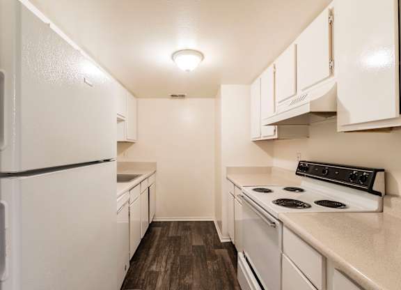 A white refrigerator is in a kitchen with a stove and cabinets.