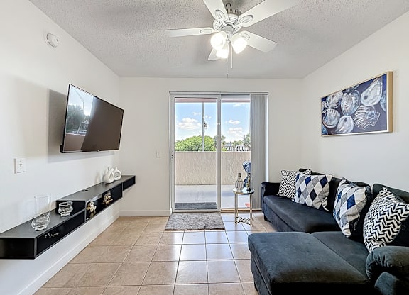 A living room with a flat screen TV mounted on the wall and a sliding glass door leading to a balcony.