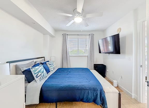 A bedroom with a blue bedspread and a flat screen TV mounted on the wall.