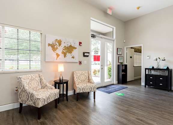 A living room with two chairs, a table with a lamp, and a world map on the wall.