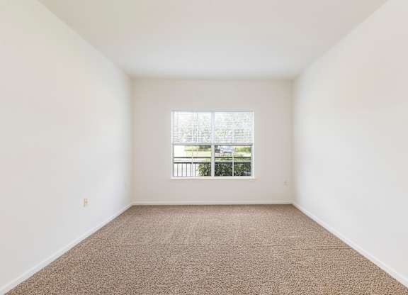 A room with a carpeted floor and a window overlooking a balcony.