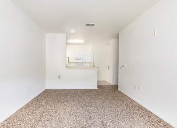 A white room with a carpeted floor and a small kitchenette in the corner.