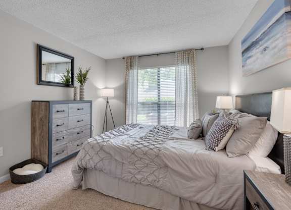 A bedroom with a bed, nightstand, and a window with curtains.