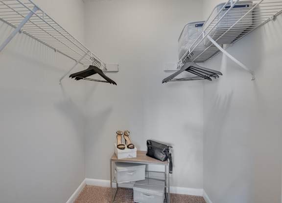 A small closet with clothes hanging and a table with shoes on it.