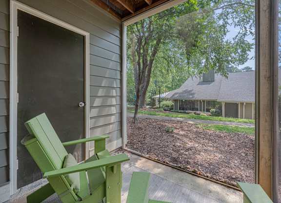 A green chair sits on a porch with a view of a house and trees.