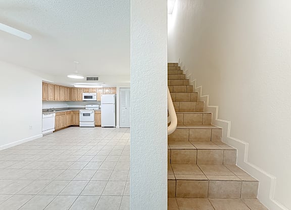 A kitchen with white appliances and a staircase.