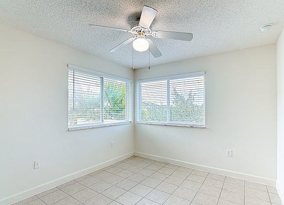 A room with a ceiling fan and two windows with blinds.