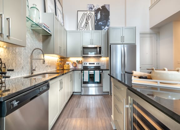 Kitchen with black quartz countertops and stainless steel appliances facing the sink and wine cooler.