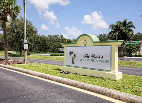 A sign for The Groves at Victoria Park is displayed in front of a tree.