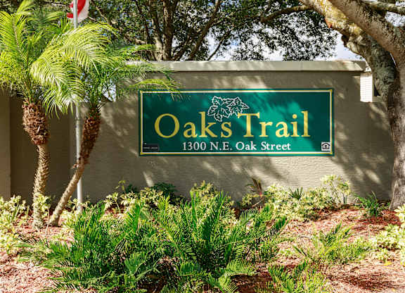 A sign for Oaks Trail stands in front of a tree.