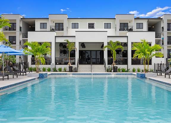 a large swimming pool in front of a building with palm trees