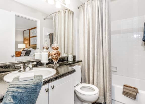 A bathroom with a white toilet, a sink, a bathtub, and a shower curtain at Paces Pointe Apartment Homes, North Carolina