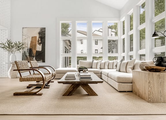 A living room with a white couch, a wooden coffee table, and a large window with a view of the outside at Paces Pointe Apartment Homes, North Carolina