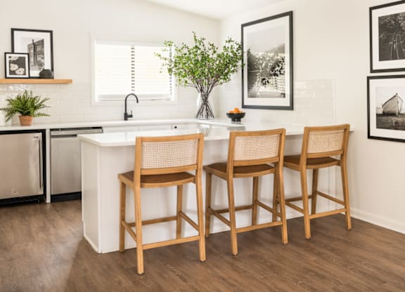 a kitchen with white countertops and a white island with three wooden chairs in front of it at The Parke at Trinity Apartment Homes, Raleigh, NC
