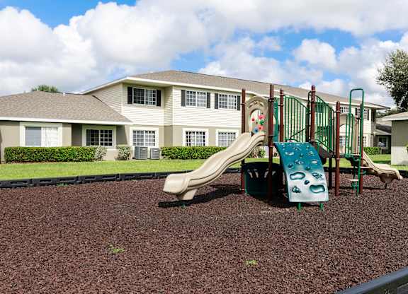 A playground with a green slide and a brown play area in front of a building.