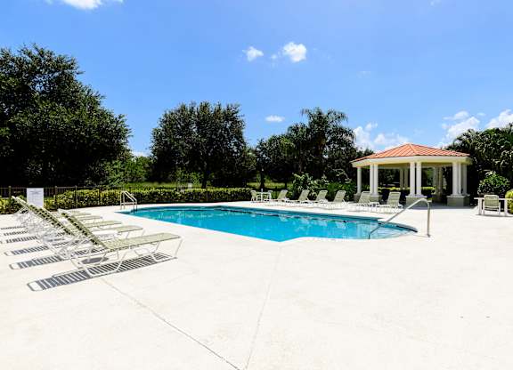A pool with sun loungers and a gazebo in the background.