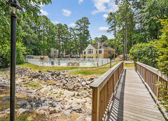 A wooden walkway leads to a house with a pool in the foreground at Regency Park Apartment Homes, Raleigh
