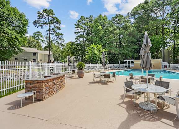 A pool area with a table and chairs and a fence at Regency Park Apartment Homes, North Carolina, 27616