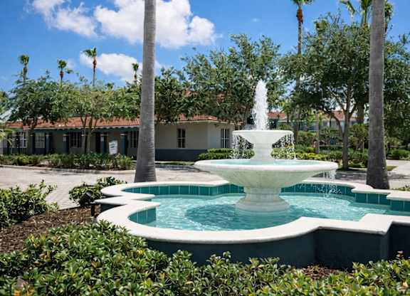 A fountain in the middle of a pool surrounded by green plants.