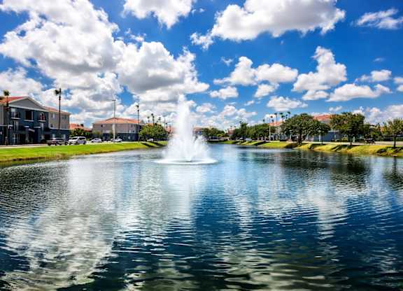 A fountain in the middle of a pond with buildings in the background.