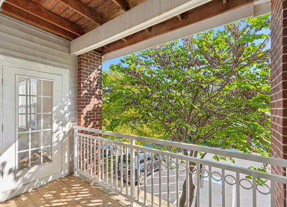 A balcony with a white railing and a view of a tree and a building.