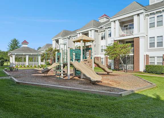 A playground with a slide and a gazebo in front of a building.