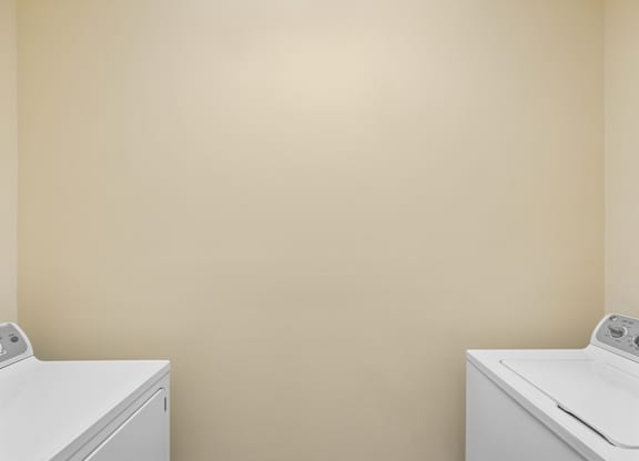 Two white washing machines in a room with beige walls.
