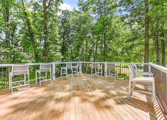 A wooden deck with white chairs and a railing overlooking a forest.