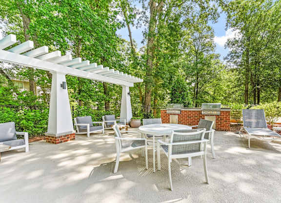 A patio with a table and chairs under a white pergola.