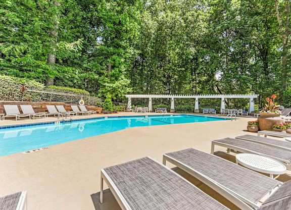 A pool surrounded by trees and lounge chairs.