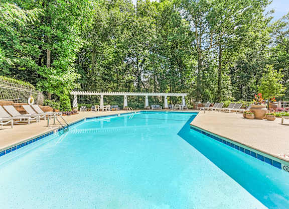 A large swimming pool surrounded by trees and lounge chairs.