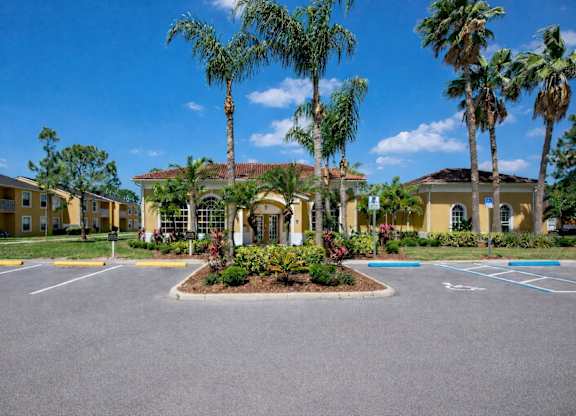 A parking lot in front of a building with palm trees.