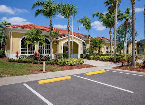 A yellow building with a red roof and palm trees in front.